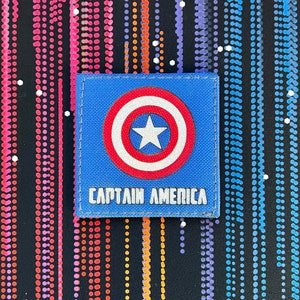 May include: A blue fabric patch with a red, white, and blue Captain America shield and the text "CAPTAIN AMERICA" in white.