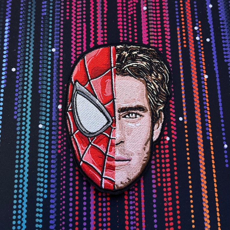 May include: Embroidered patch featuring a split image of Spider-Man's mask and Tom Holland's face. The mask is red and blue with a white spider design. The face is a realistic portrait with brown hair.