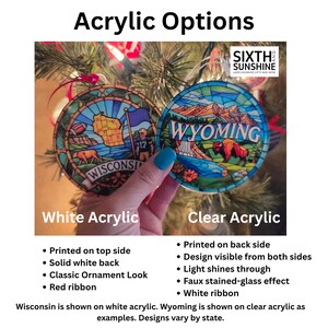 May include: Two round acrylic ornaments featuring stained-glass style designs of Wisconsin and Wyoming. The Wisconsin ornament is on white acrylic with a red ribbon, while the Wyoming ornament is on clear acrylic with a white ribbon.