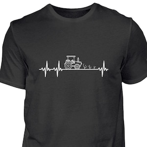 Könnte beinhalten: Schwarzes T-Shirt mit einer weißen Grafik eines Traktors, der durch ein Feld fährt, mit einer Herzschlaglinie darüber.
