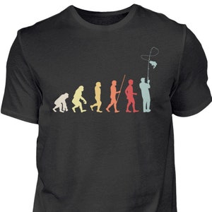 Könnte beinhalten: Ein schwarzes T-Shirt mit einer Illustration im Vintage-Stil der Evolution des Menschen, die in einer Person beim Angeln gipfelt. Die Illustration ist in Rot-, Orange-, Gelb-, Grün- und Blautönen gehalten.