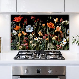 May include: A rectangular kitchen backsplash panel featuring a vibrant botanical print of various wildflowers including orange poppies, white daisies, and small red blossoms set against a solid black background, positioned behind a stainless steel stove.