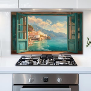 May include: A framed wall art print depicting an open window with teal shutters overlooking a coastal town and turquoise sea. The artwork is displayed above a stainless steel gas stovetop.