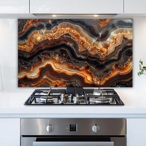 May include: A decorative kitchen backsplash featuring a layered agate design. The artwork showcases bands of brown, black, and gold, creating a natural, abstract pattern. The backsplash is mounted above a gas stovetop.