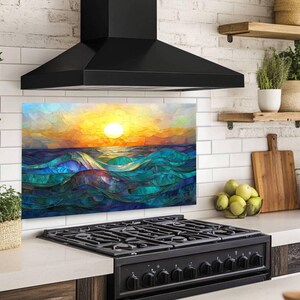 A stained-glass style backsplash featuring an ocean sunset with rolling waves is set on a white subway tile wall. It sits beneath a black hood and behind a black range, flanked by open shelves with plants and fruit.