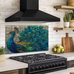 Vibrant peacock stained glass kitchen backsplash with shades of blue and teal. The artistic panel is mounted behind a professional black gas range in a kitchen with large-format beige marble wall tiles and a stainless steel range hood.