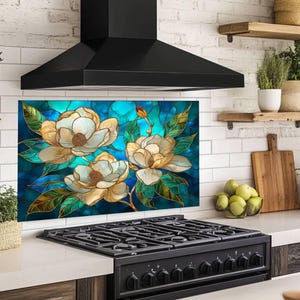 Stained glass style backsplash featuring three large cream-colored magnolias with green leaves on a vibrant blue and turquoise background, installed behind a black gas range in a white brick kitchen with wooden shelving.