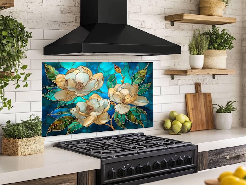 Stained glass style backsplash featuring three large cream-colored magnolias with green leaves on a vibrant blue and turquoise background, installed behind a black gas range in a white brick kitchen with wooden shelving.