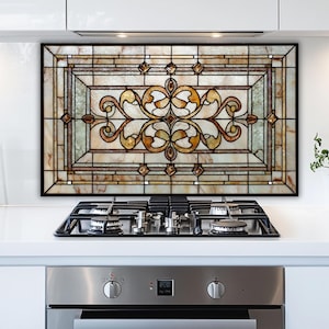 May include: A decorative kitchen backsplash with a stained glass design. The rectangular panel features a black frame and a central ornate pattern in shades of brown, gold, and cream. The backsplash is mounted above a gas stovetop.