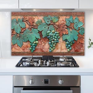 May include: A decorative kitchen backsplash featuring a relief of grape vines with green leaves and bunches of grapes. The background has a marble-like texture with shades of red, brown, and beige.
