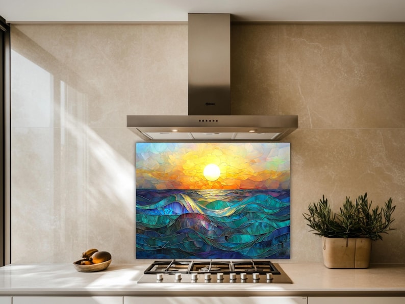 A stained-glass style backsplash featuring an ocean sunset with rolling waves is set in a modern kitchen with beige stone walls. It sits behind a gas cooktop, flanked by a fruit bowl and a potted plant.