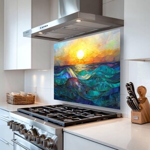A stained-glass style backsplash featuring an ocean sunset with rolling waves is displayed in a modern white kitchen. It sits behind a gas cooktop, flanked by a woven basket and a knife block.