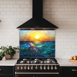A stained-glass style backsplash featuring an ocean sunset with rolling waves is set in a kitchen with white subway tiles and black cabinets. It sits beneath a black hood, flanked by a plant and fresh produce.