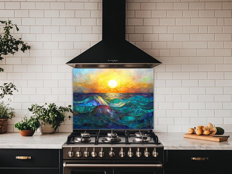 A stained-glass style backsplash featuring an ocean sunset with rolling waves is set in a kitchen with white subway tiles and black cabinets. It sits beneath a black hood, flanked by a plant and fresh produce.