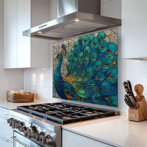 Vibrant peacock stained-glass backsplash in shades of teal and blue, mounted behind a professional gas range in a sleek white kitchen with a stainless steel hood and minimalist white cabinetry.