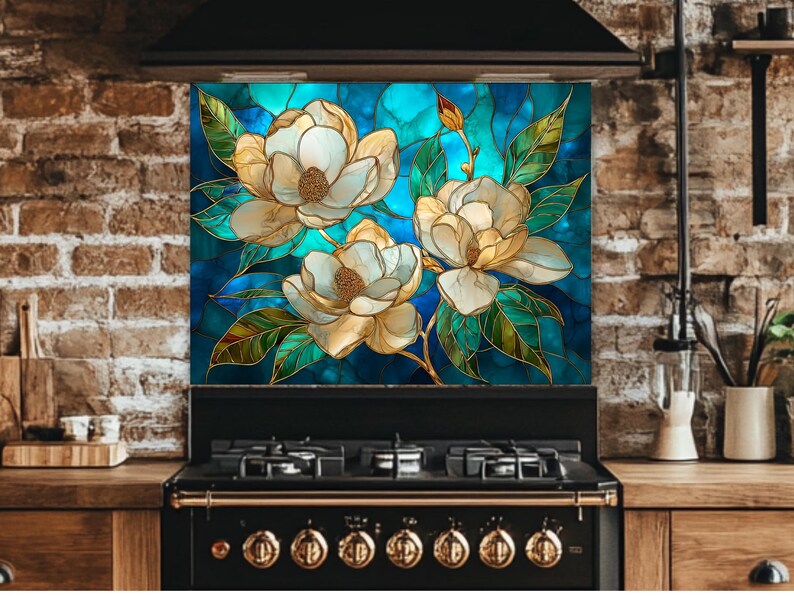 Stained glass style backsplash featuring three large cream-colored magnolias with green leaves on a vibrant blue and turquoise background, installed behind a black gas range in a rustic brick kitchen.