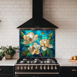 Stained glass style backsplash featuring three cream magnolias on a vibrant turquoise background, installed behind a black gas range in a white subway-tiled kitchen with dark cabinetry.