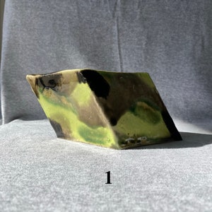 May include: A ceramic, angular vase with a camouflage pattern in shades of green, brown, and black. The vase has a glossy finish and the number "1" is printed on the front. The vase is set against a gray background.