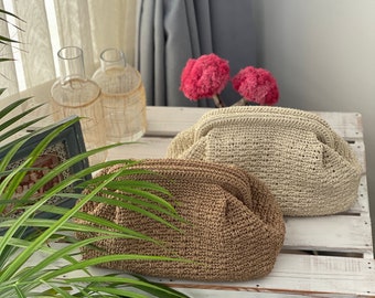 Puede incluir: Dos bolsos de mano tejidos, beige y marrón, sobre una superficie de madera blanca. Los bolsos tienen un diseño fruncido. El fondo incluye una ventana con cortinas transparentes, jarrones decorativos y acentos florales rosas.