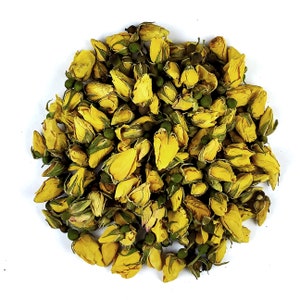 Op de afbeelding: Een close-up van een stapel gedroogde gele rozenknoppen. De knoppen zijn in een cirkelvormige opstelling gerangschikt en worden omringd door groene bladeren.