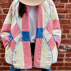 Puede incluir: Un sombrero beige con una banda floral y una chaqueta acolchada en colores rosa, azul y crema. La chaqueta tiene un diseño de patchwork único y se usa sobre una camiseta blanca y vaqueros azules. El conjunto se completa con botines beige.