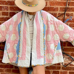 Puede incluir: Un sombrero beige de ala ancha con una banda floral, una chaqueta acolchada con un patrón de parches hexagonales en rosa, blanco y azul con ribete floral, una camisa blanca y botas vaqueras de cuero azul claro con costuras detalladas.
