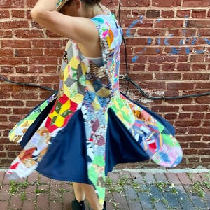 Può includere: Un colorato vestito patchwork con una gonna blu navy. L'abito presenta una varietà di motivi e colori di tessuto, tra cui rosso, giallo e blu. La persona indossa stivali neri e un cappello abbinato.