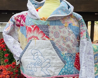 May include: A patchwork hoodie in various floral and geometric patterns, featuring blue, red, and white hues. The front pocket has a blue embroidered design. The hoodie is displayed on a mannequin.
