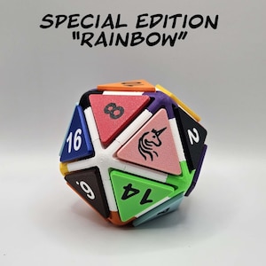 May include: A multi-colored, geometric die with triangular faces, each displaying a number or a unicorn graphic. The text "SPECIAL EDITION 'RAINBOW'" is above the die. The die's colors include blue, green, pink, red, and black.