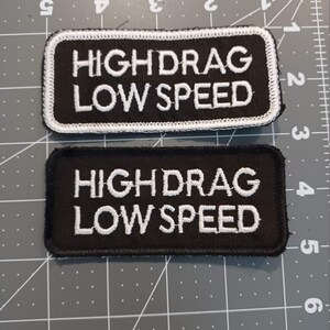 May include: Two black embroidered patches with white stitching. The patches read "HIGH DRAG LOW SPEED".