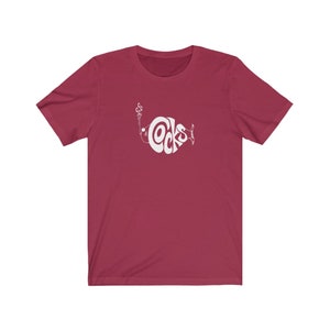 May include: A maroon t-shirt with a white graphic of a fish with the word "Cocks" inside the fish.