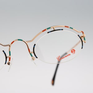 May include: Gold-tone eyeglasses with a round frame and colorful accents. The brand name "Casanova" is printed on the right lens.