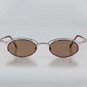 May include: Silver oval-shaped sunglasses with brown lenses and a tortoiseshell pattern on the frame.