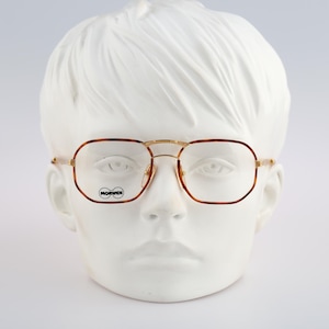 May include: A pair of gold-rimmed glasses with brown tortoise shell frames. The glasses are on a white mannequin head. The brand name "MORMAII" is visible on the left lens.