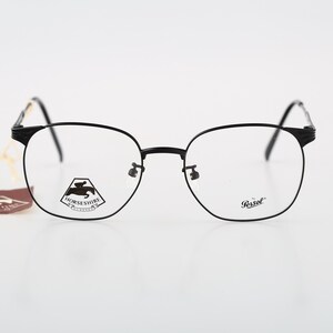 Puede incluir: Gafas con montura de metal negro y lentes transparentes. La lente izquierda tiene una pegatina blanca con un logotipo de caballo negro y el texto HORSESHIRE. La lente derecha lleva el logotipo de Persol. Una etiqueta marrón está unida.