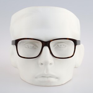 May include: Rectangular eyeglasses with a dark brown tortoiseshell pattern frame. The glasses feature clear lenses and are displayed on a white mannequin head, showcasing the classic shape and the mottled brown and black color of the frame.