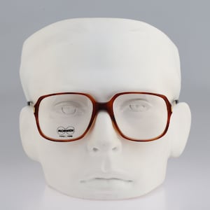 May include: Brown tortoiseshell eyeglasses with a gold metal frame and clear lenses. The glasses are on a white mannequin head. The brand name "MORRIS" is printed on the left lens.