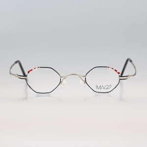 Op de afbeelding: Zwarte en zilveren, achthoekige bril met rode accenten op het montuur. De merknaam "IMAGO" is op de rechterlens gedrukt.