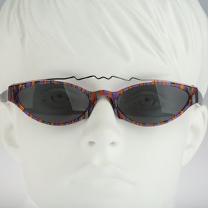 Puede incluir: Gafas de sol rayadas de color morado y naranja con montura de metal negro. Las gafas tienen un diseño único y curvado.