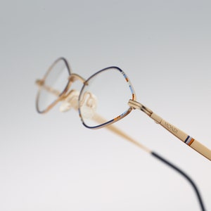 May include: Gold-tone eyeglasses with blue and orange accents on the arms. The brand name "MONDI" is printed on the right arm.