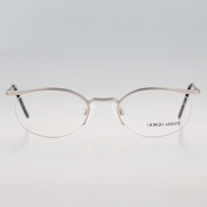 May include: Silver-toned semi-rimless eyeglasses featuring a thin metal frame with a textured top brow bar. The clear lenses are etched with the Giorgio Armani brand name on the right side. The design includes slender temples and nose pads.