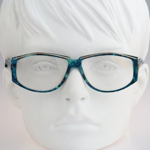 Könnte beinhalten: Eine Brille in blaugrüner Farbe mit goldfarbenem Rahmen auf einem weißen Mannequin-Kopf.