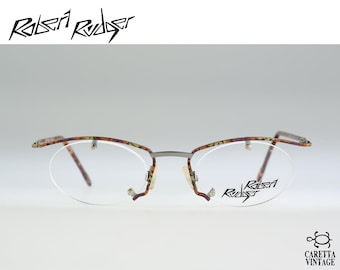 May include: Robert Rudger semi-rimless eyeglasses featuring a brown and gold tortoiseshell pattern on the upper frame and temples. The lenses are oval-shaped and clear, with the brand name Robert Rudger printed in black on the right lens.