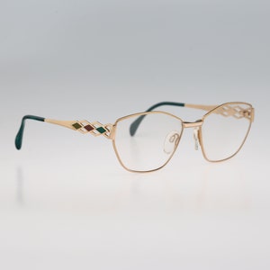 Könnte beinhalten: Goldfarbene Brille mit geometrischem Design. Die Fassungen haben ein Rautenmuster an den Bügeln mit grünen, roten und weißen Akzenten. Die Gläser sind klar und die Bügel sind dunkelgrün.
