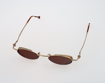 May include: Gold-tone metal oval-shaped sunglasses with brown lenses. The sunglasses have thin metal arms.