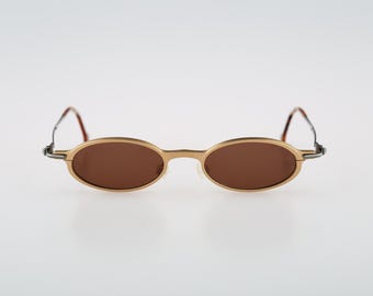 May include: Gold-tone oval-shaped sunglasses with brown lenses. The sunglasses have a thin metal frame.