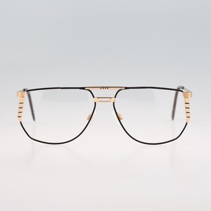 May include: Black metal frame glasses with gold accents on the arms. The glasses have a rectangular shape and clear lenses.