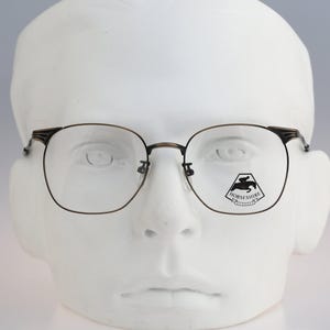 Puede incluir: Gafas de tono metálico oscuro con una montura fina y rectangular y almohadillas nasales ajustables. El cristal derecho presenta un logotipo negro impreso de un caballo y un jinete con el texto HORSESHIRE debajo, dentro de un contorno.