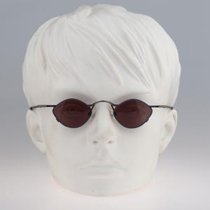 Puede incluir: Un par de gafas de sol ovaladas con lentes de color marrón oscuro y un fino marco de metal.