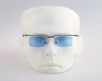 May include: Rectangular eyeglasses featuring light blue tinted lenses and a thin, dark metallic frame. The design includes a straight top bar connecting the two lenses, with adjustable nose pads and slender temples extending from the sides.